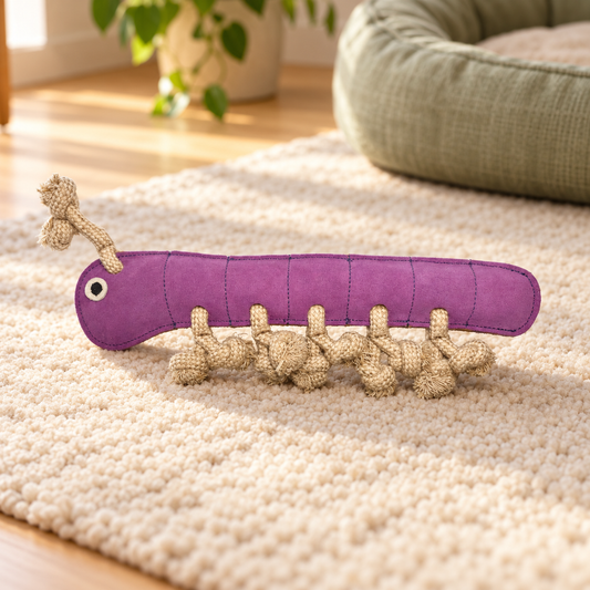Purple Georgie Paws Gerti the Grub leather dog toy with knotted rope legs on a cream rug in a softly lit home